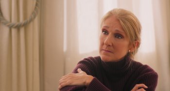 Movie still from “Love Again” (2023), directed by Jim Strouse – A woman sitting in front of a window with her arms crossed; Close Up shot, Over the shoulder angle