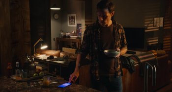 Movie still from “Love Again” (2023), directed by Jim Strouse – A man is holding a pan and a cell phone; Medium shot, Over the shoulder angle