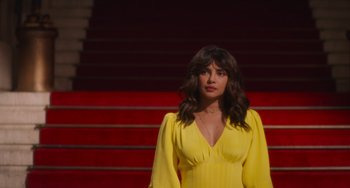 Movie still from “Love Again” (2023), directed by Jim Strouse – A woman in a yellow dress standing in front of red stairs; Medium shot, Low angle