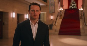 Movie still from “Love Again” (2023), directed by Jim Strouse – A man in a suit standing in front of a staircase; Medium shot, Over the shoulder angle