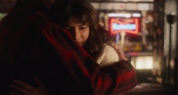 Movie still from “Love Again” (2023), directed by Jim Strouse – A woman hugging a man in a red and black plaid jacket; Close Up shot, Over the shoulder angle