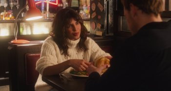 Movie still from “Love Again” (2023), directed by Jim Strouse – A woman sitting at a table in front of a plate of food; Medium shot, Over the shoulder angle