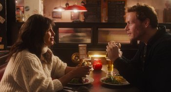 Movie still from “Love Again” (2023), directed by Jim Strouse – A man and a woman sitting at a table with a plate of food; Medium shot, Over the shoulder angle