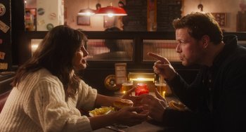 Movie still from “Love Again” (2023), directed by Jim Strouse – A man and a woman sitting at a table; Medium shot, Over the shoulder angle