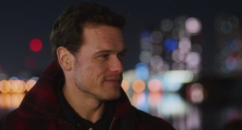 Movie still from “Love Again” (2023), directed by Jim Strouse – A person wearing a jacket with lights in the background; Close Up shot, Over the shoulder angle