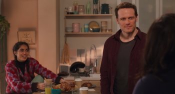 Movie still from “Love Again” (2023), directed by Jim Strouse – A man standing in front of a table with food on top of it; Medium shot, Over the shoulder angle