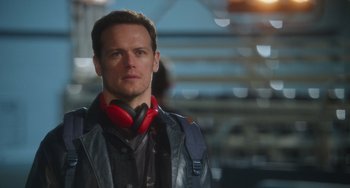 Movie still from “Love Again” (2023), directed by Jim Strouse – A man with red headphones standing in front of a building; Close Up shot, Over the shoulder angle