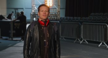 Movie still from “Love Again” (2023), directed by Jim Strouse – A man wearing a black jacket and red headphones; Medium shot, Over the shoulder angle