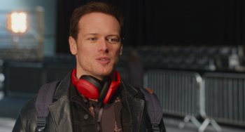 Movie still from “Love Again” (2023), directed by Jim Strouse – A person wearing headphones and a jacket; Close Up shot, Over the shoulder angle