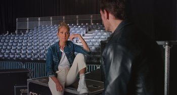Movie still from “Love Again” (2023), directed by Jim Strouse – A man and a woman sitting in front of each other in front of an audience; Wide shot, Over the shoulder angle