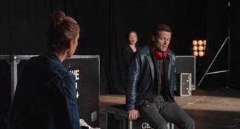 Movie still from “Love Again” (2023), directed by Jim Strouse – A man and a woman wearing headphones in front of another man; Medium shot, Over the shoulder angle