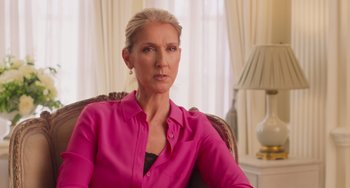 Movie still from “Love Again” (2023), directed by Jim Strouse – A woman sitting in a chair wearing a pink shirt; Close Up shot, Over the shoulder angle