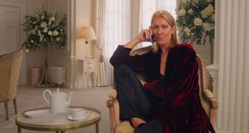 Movie still from “Love Again” (2023), directed by Jim Strouse – A woman sitting in a chair talking on a phone; Medium shot, Over the shoulder angle