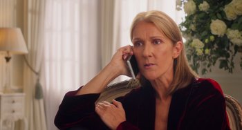 Movie still from “Love Again” (2023), directed by Jim Strouse – A woman talking on a cell phone while sitting on a couch; Close Up shot, Over the shoulder angle
