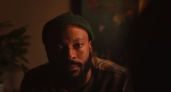 Movie still from “Love Again” (2023), directed by Jim Strouse – A man with a beard wearing a green hat; Close Up shot, Low angle