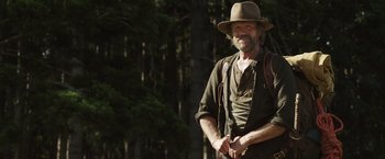 Movie still from “Love and Monsters” (2020), directed by Michael Matthews – A man with a beard and a hat is smiling for the camera; Medium shot, Over the shoulder angle