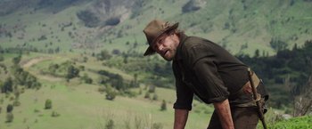Movie still from “Love and Monsters” (2020), directed by Michael Matthews – A man in a hat is standing in a field; Medium shot, Over the shoulder angle
