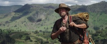 Movie still from “Love and Monsters” (2020), directed by Michael Matthews – A man with a beard wearing a hat and holding a backpack; Medium shot, Over the shoulder angle