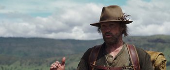 Movie still from “Love and Monsters” (2020), directed by Michael Matthews – A man wearing a hat is standing in front of a mountain; Close Up shot, Over the shoulder angle