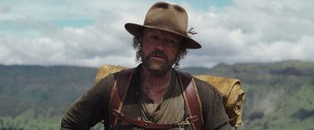 Movie still from “Love and Monsters” (2020), directed by Michael Matthews – A man wearing a hat and leather suspenders; Close Up shot, Low angle