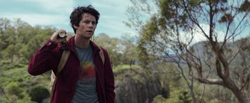 Movie still from “Love and Monsters” (2020), directed by Michael Matthews – A man standing in front of a tree with trees in the background; Medium shot, Over the shoulder angle
