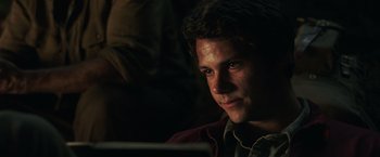 Movie still from “Love and Monsters” (2020), directed by Michael Matthews – A young man looking at the camera while sitting in a dark room; Close Up shot, Over the shoulder angle