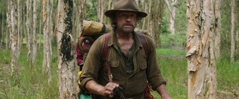 Movie still from “Love and Monsters” (2020), directed by Michael Matthews – A man with a hat and a backpack walking through the woods; Medium shot, Over the shoulder angle