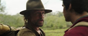 Movie still from “Love and Monsters” (2020), directed by Michael Matthews – A person wearing a hat with trees in the background; Close Up shot, Over the shoulder angle