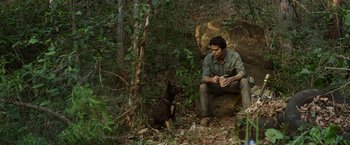 Movie still from “Love and Monsters” (2020), directed by Michael Matthews – A man sitting on a rock next to a brown dog; Wide shot, High angle