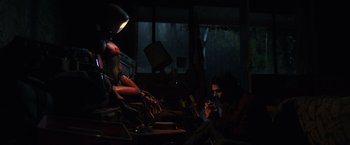 Movie still from “Love and Monsters” (2020), directed by Michael Matthews – A man sitting at a table in a dark room; Wide shot, Low angle