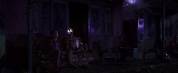 Movie still from “Love and Monsters” (2020), directed by Michael Matthews – A man sitting on a couch next to a robot; Wide shot, Low angle