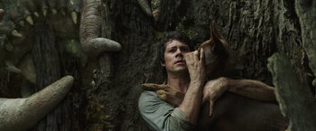 Movie still from “Love and Monsters” (2020), directed by Michael Matthews – A man holding a dog while standing next to a tree; Close Up shot, Overhead angle