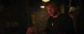 Movie still from “Love and Monsters” (2020), directed by Michael Matthews – A man with a beard and a necklace in a dark room; Close Up shot, Over the shoulder angle