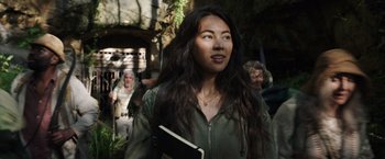 Movie still from “Love and Monsters” (2020), directed by Michael Matthews – A woman holding a book while standing next to a group of people; Close Up shot, Low angle