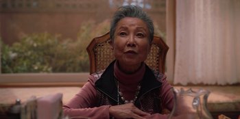 Movie still from “Love Hard” (2021), directed by Hernán Jiménez – An older woman sitting at a table in front of a window; Close Up shot, Over the shoulder angle