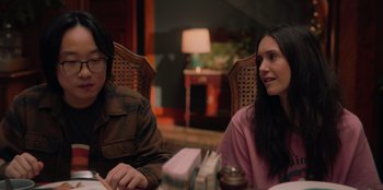 Movie still from “Love Hard” (2021), directed by Hernán Jiménez – Two people are sitting at a table and one is reading a book; Medium shot, Over the shoulder angle