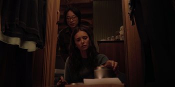 Movie still from “Love Hard” (2021), directed by Hernán Jiménez – A woman sitting at a table with another woman standing next to her; Medium shot, Over the shoulder angle