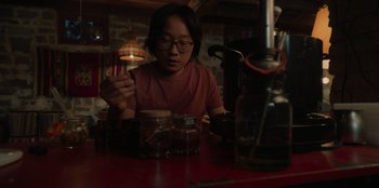 Movie still from “Love Hard” (2021), directed by Hernán Jiménez – A person sitting at a table with a jar of food; Medium shot, High angle