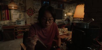 Movie still from “Love Hard” (2021), directed by Hernán Jiménez – A person sitting at a table with a bowl and chopsticks in front of him; Medium shot, Over the shoulder angle