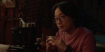 Movie still from “Love Hard” (2021), directed by Hernán Jiménez – A person sitting at a table with a cup of coffee; Close Up shot, Over the shoulder angle