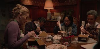 Movie still from “Love Hard” (2021), directed by Hernán Jiménez – A group of people sitting at a table making gingerbread houses; Medium shot, High angle