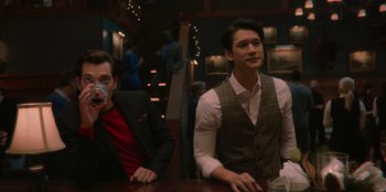 Movie still from “Love Hard” (2021), directed by Hernán Jiménez – Two men sitting at a table in front of a bar; Medium shot, Over the shoulder angle