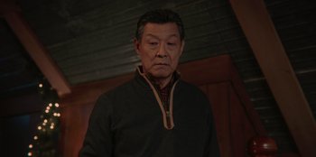 Movie still from “Love Hard” (2021), directed by Hernán Jiménez – An older asian man wearing a black jacket; Close Up shot, Low angle