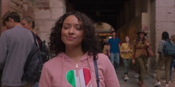 Movie still from “Love in the Villa” (2022), directed by Mark Steven Johnson – A young woman with a heart on her shirt is standing in front of a crowd; Close Up shot, Over the shoulder angle