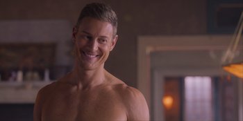 Movie still from “Love in the Villa” (2022), directed by Mark Steven Johnson – A man with no shirt smiling for the camera; Close Up shot, Over the shoulder angle