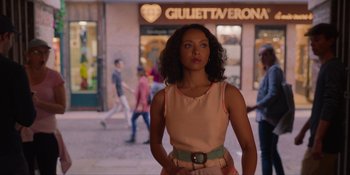 Movie still from “Love in the Villa” (2022), directed by Mark Steven Johnson – A woman standing in front of a store on the sidewalk; Medium shot, Over the shoulder angle