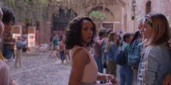 Movie still from “Love in the Villa” (2022), directed by Mark Steven Johnson – A woman standing in front of a group of people; Medium shot, Over the shoulder angle