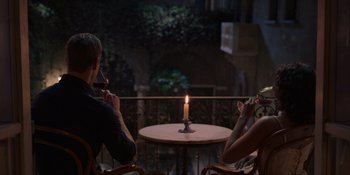 Movie still from “Love in the Villa” (2022), directed by Mark Steven Johnson – Two people sitting at a table with a lit candle in the middle; Wide shot, Over the shoulder angle