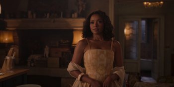 Movie still from “Love in the Villa” (2022), directed by Mark Steven Johnson – A woman in a dress standing next to a fireplace; Medium shot, Over the shoulder angle