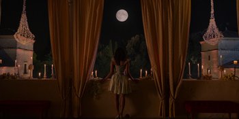 Movie still from “Love in the Villa” (2022), directed by Mark Steven Johnson – A woman standing in front of a window at night with candles; Extreme Wide shot, Low angle
